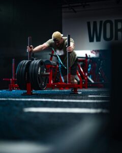 A man in a gym pushes a weighted sled, showcasing strength training and fitness determination.